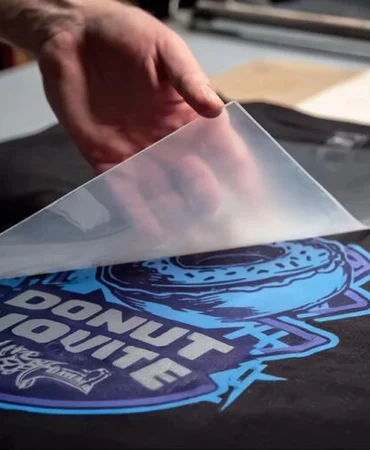 One of our production associates peeling a DTR (Direct-To-Film) transfer sheet off of a newly heat-pressed t-shirt